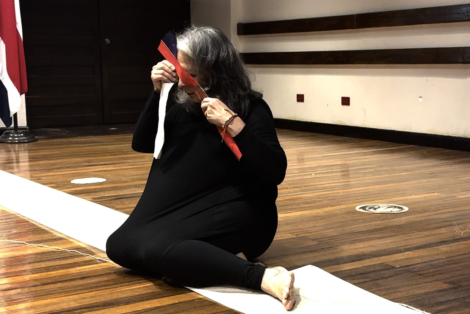 Convergences, 2025, performance: the artist on the floor with red and white strips of paper
